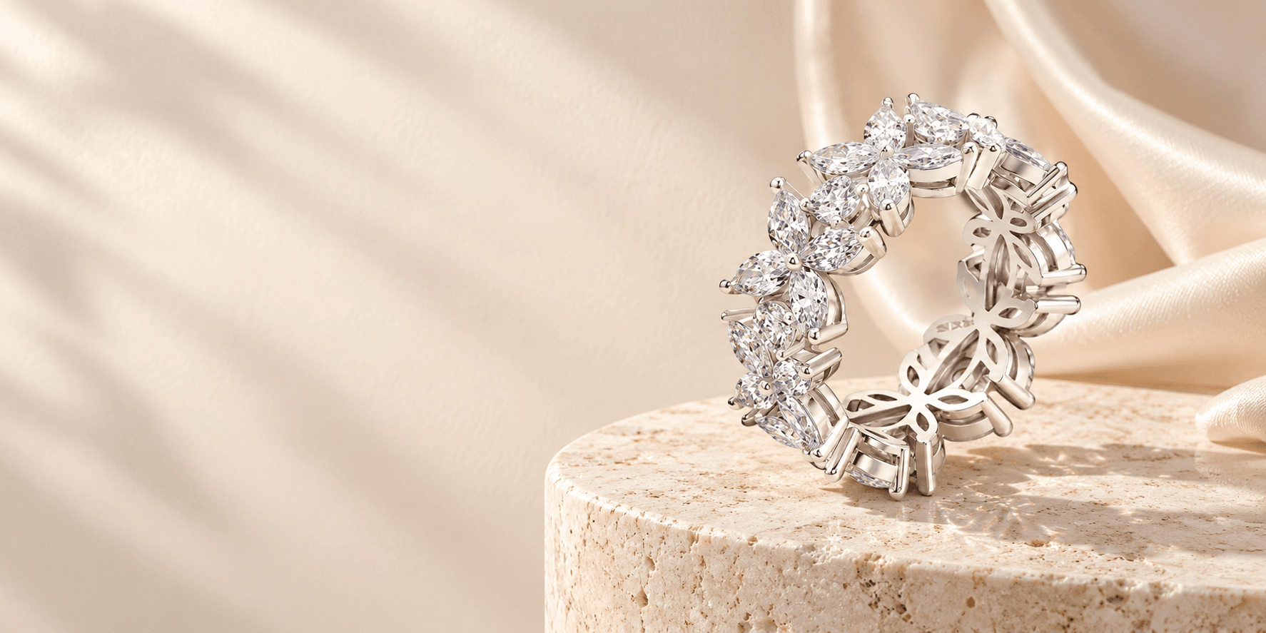 A floral silver ring on warm travertine, surrounded by ivory silk